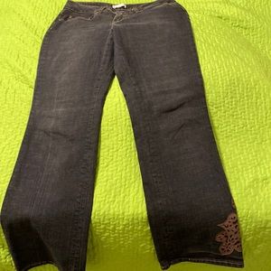 Dark blue jeans with brown pattern on pockets and left leg by ankle